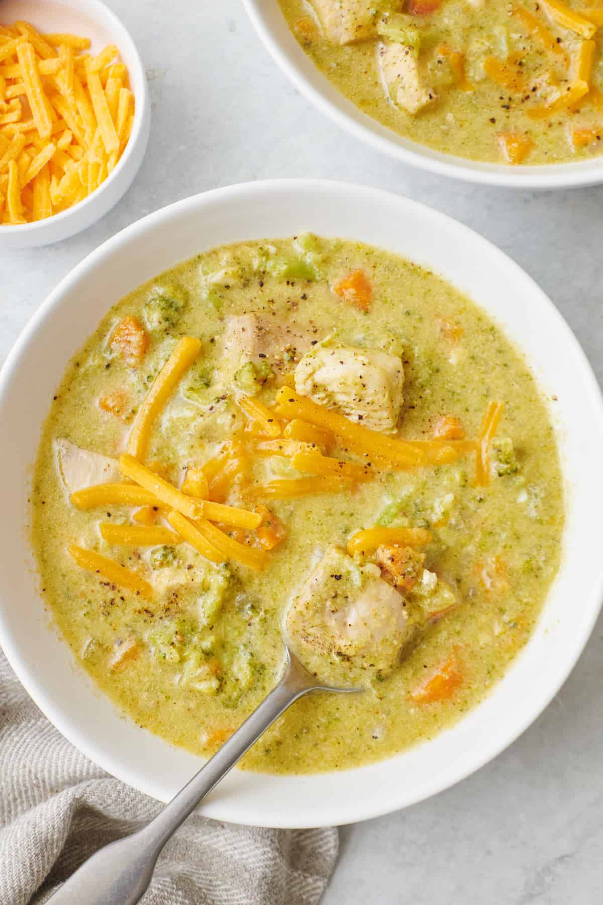 Spoon lifting up a bite of cheesy chicken broccoli soup from a bowl.