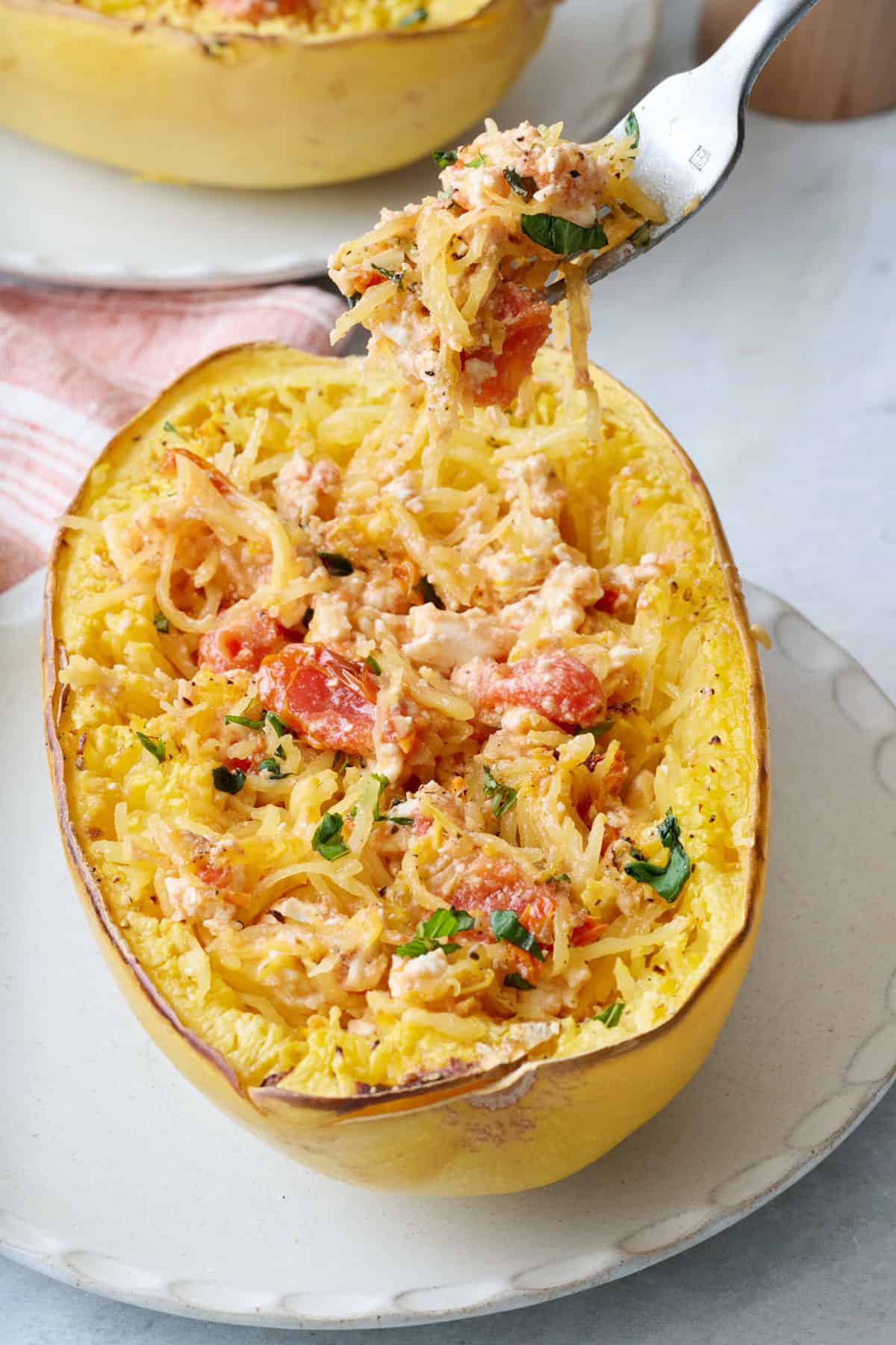 Closeup of a fork scooping up a baked feta spaghetti squash with cherry tomatoes and garlic.