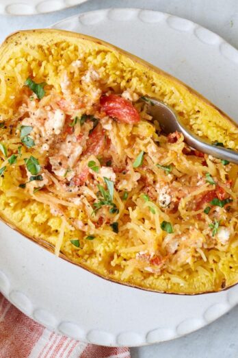 A fork scooping from a feta spaghetti squash made with cherry tomatoes and garlic on a white round plate.