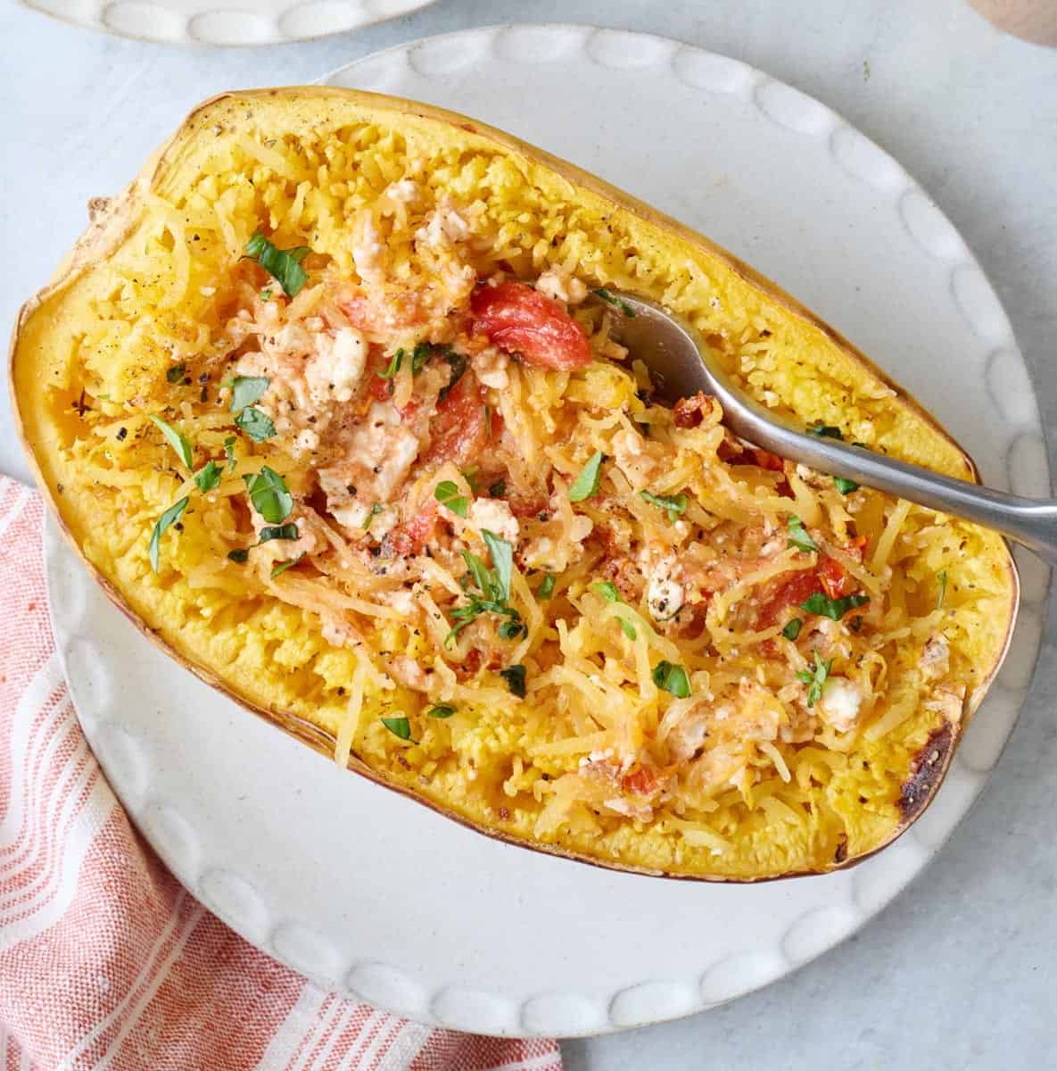 A fork scooping from a feta spaghetti squash made with cherry tomatoes and garlic on a white round plate.