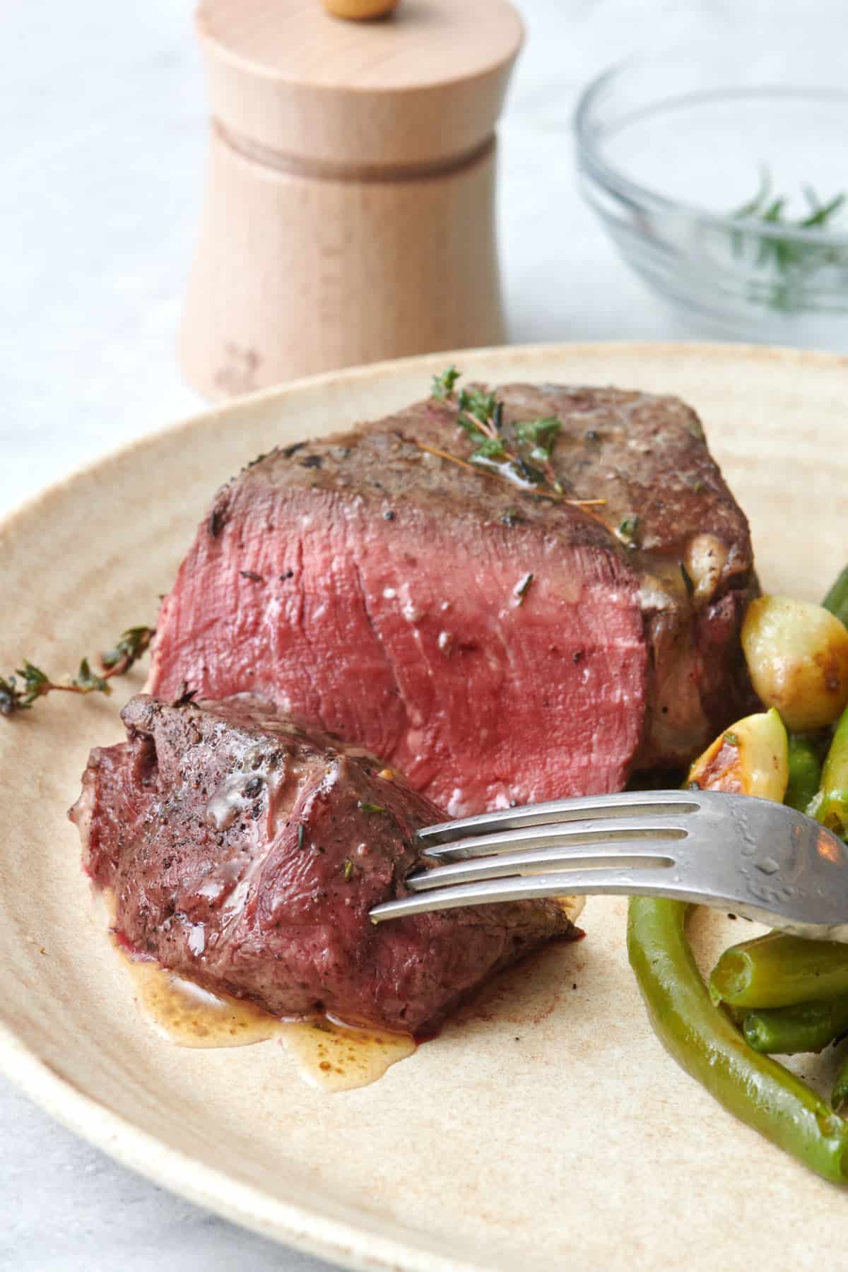 Filet mignon cooked medium rare on a plate with a piece cut away and a fork lifting it up.