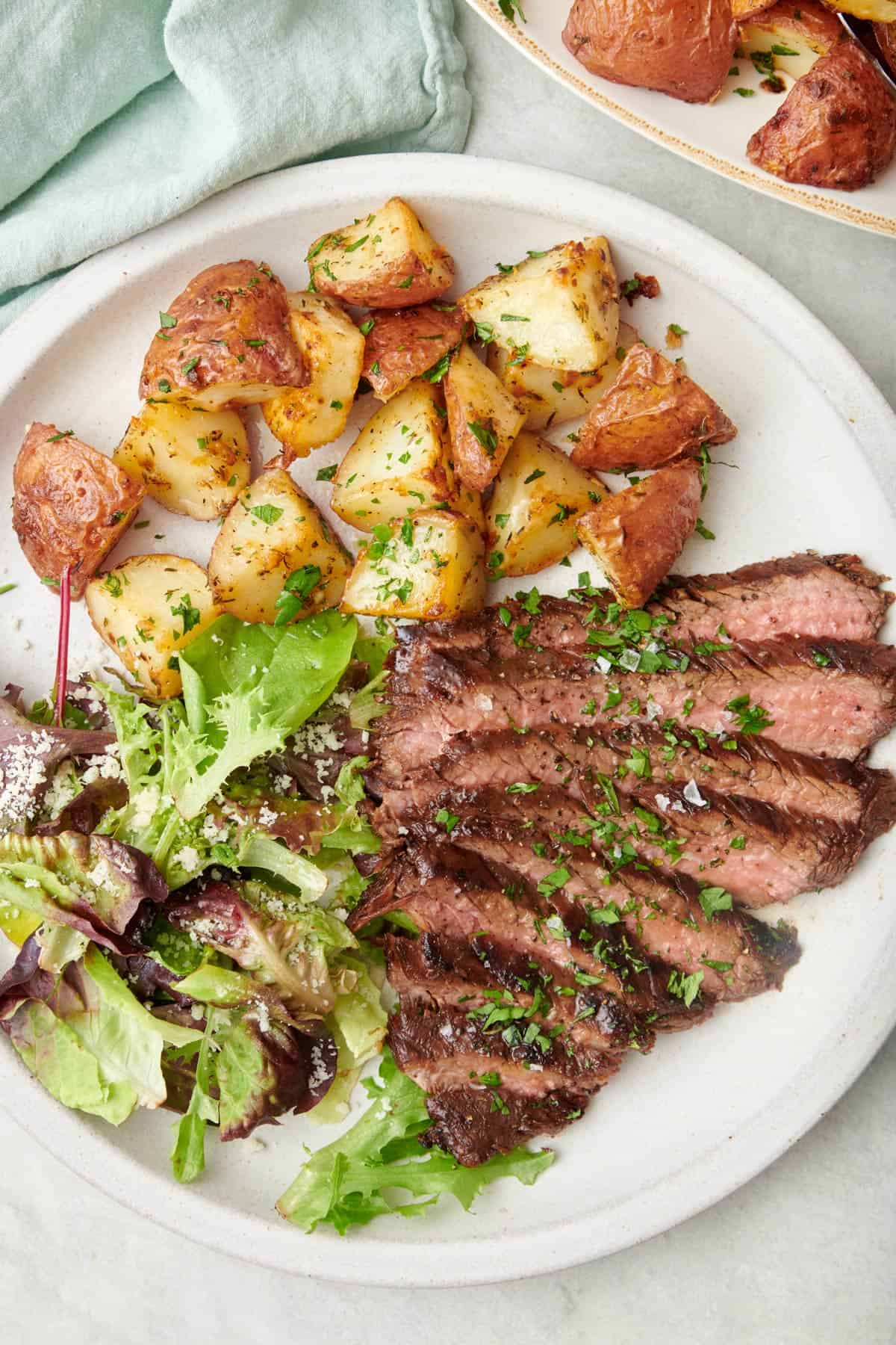 Sliced flank steak on a plate with potatoes and a light salad.