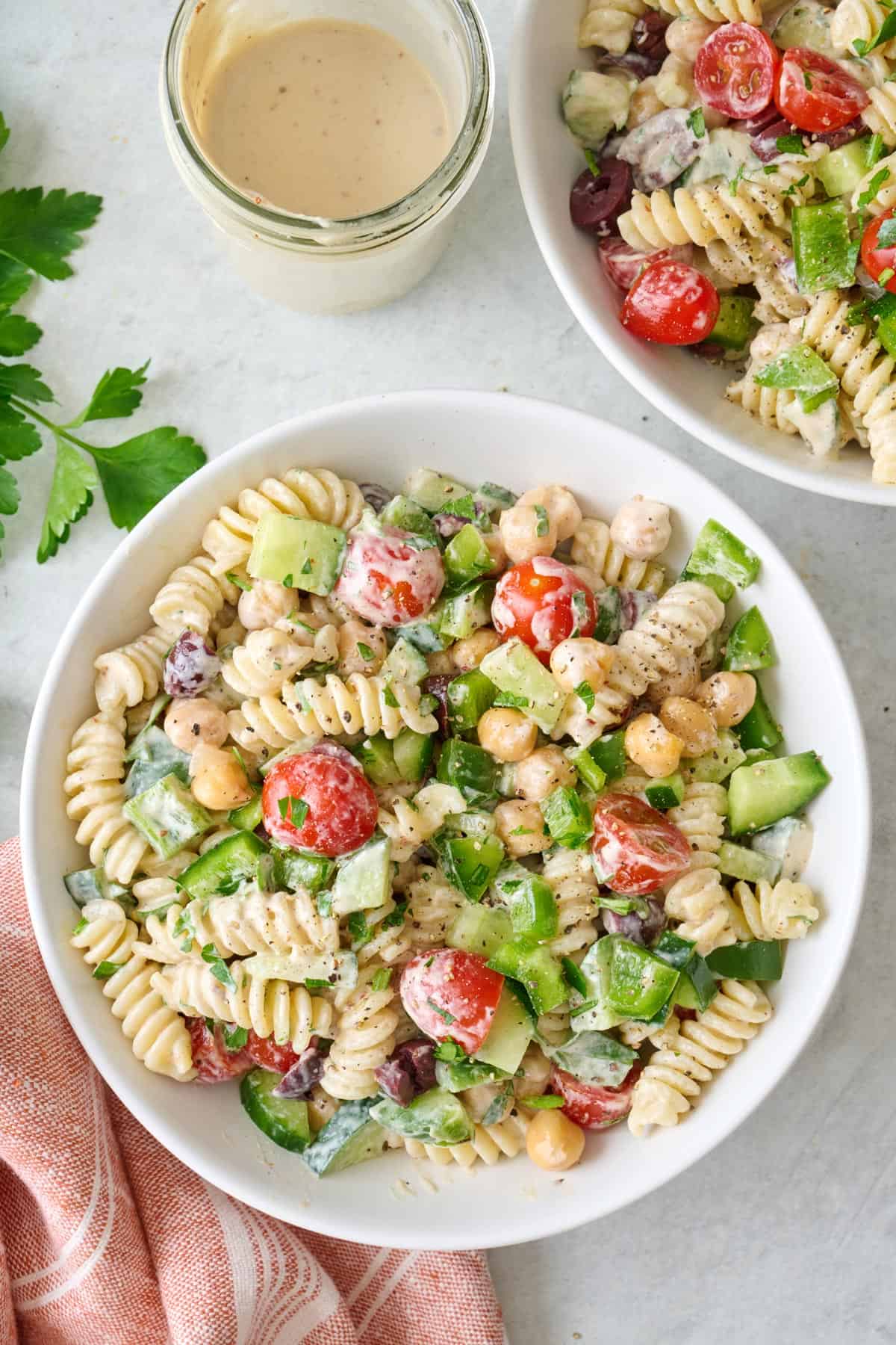 Overhead of a small bowl of tahini pasta salad with dressing and a serving bowl of the salad nearby.