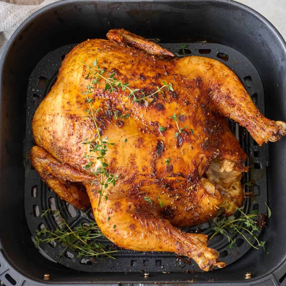 Whole chicken in air fryer after cooking, garnished with fresh thyme.
