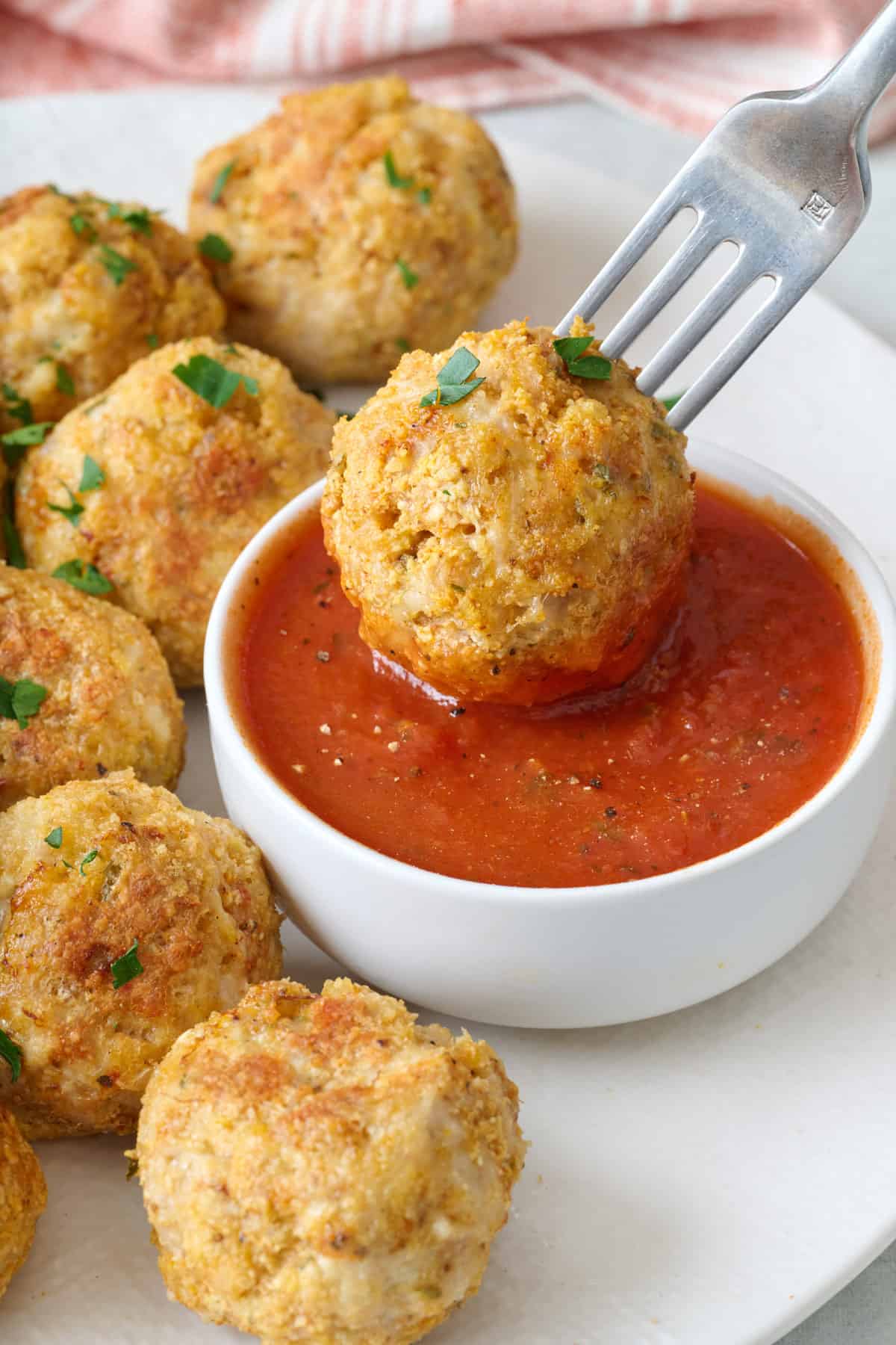 Fork dipping a chicken meatball into marinara sauce with more meatballs on the plate.