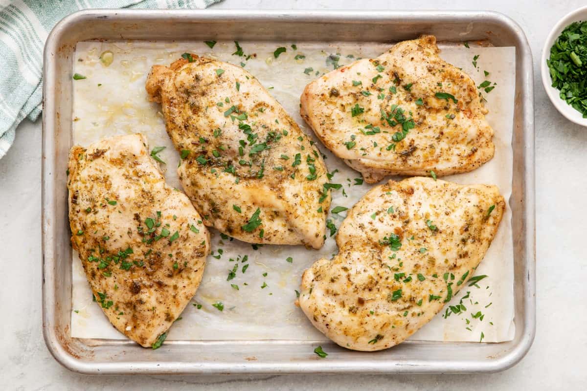 Baked chicken on baking sheet garnished with fresh parsley