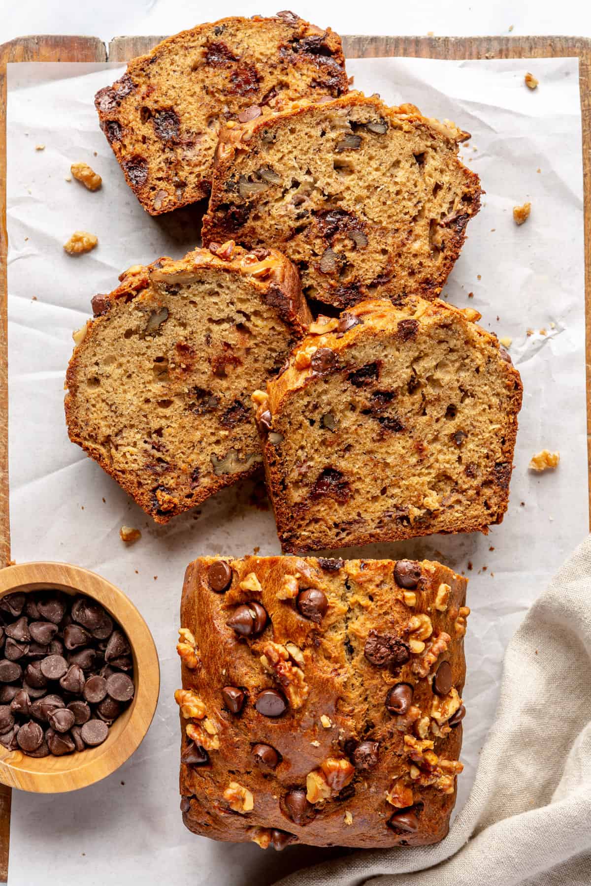 Chocolate chip banana bread on parchment paper with a few slices cut away from the loaf and staggered to show the cut side.