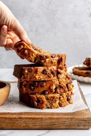 Chocolate chip banana bread slices stacked up with a hand lifting up the top piece.