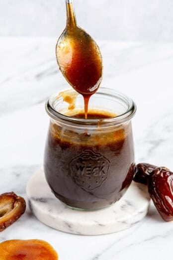 Spoon lifting up date syrup from the jar drizzling it back into it.
