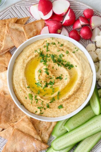 Homemade hummus recipe without tahini served with pita chips, cucumber, cauliflower, and radishes.