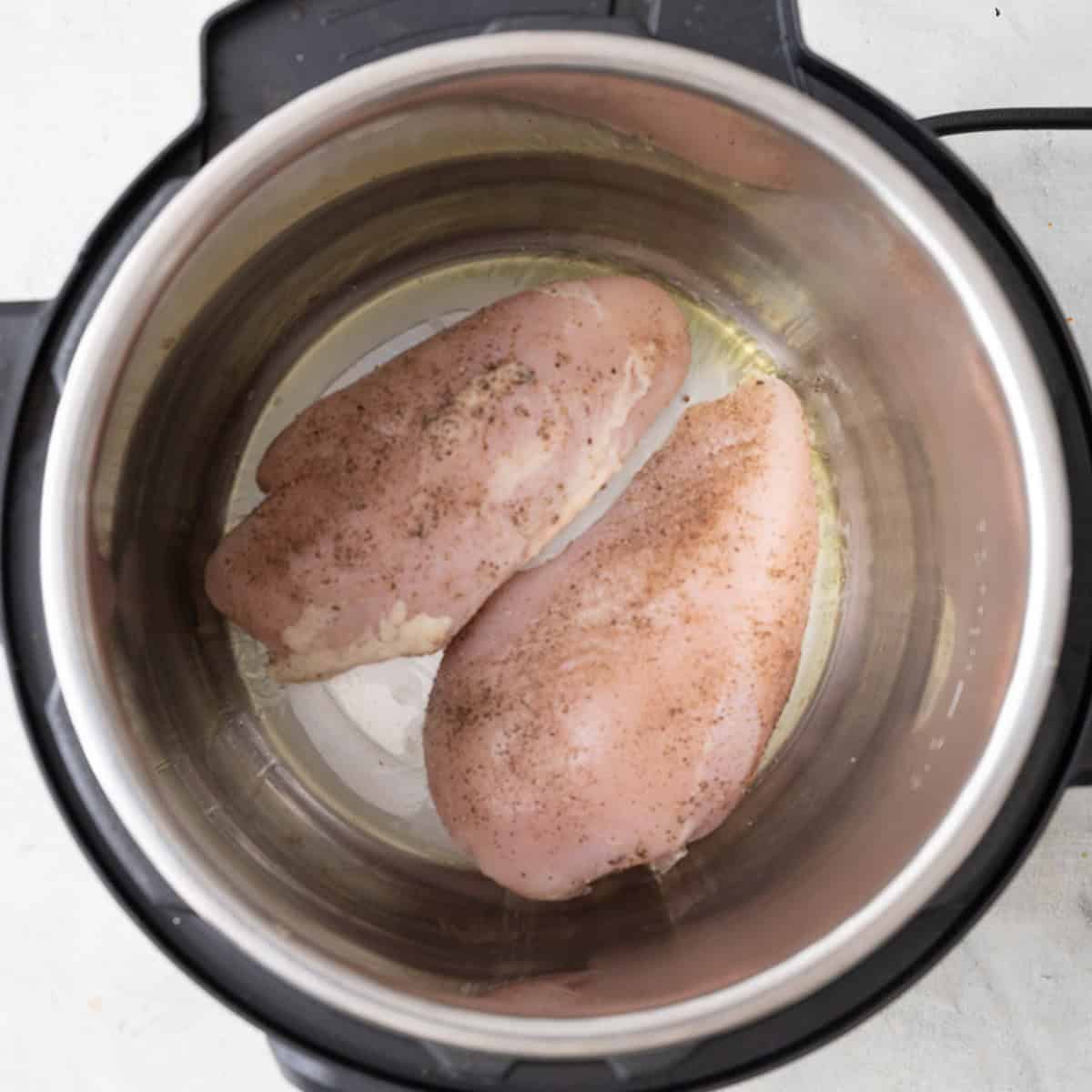 Oil, chicken, and seasonings in an IP before cooking.