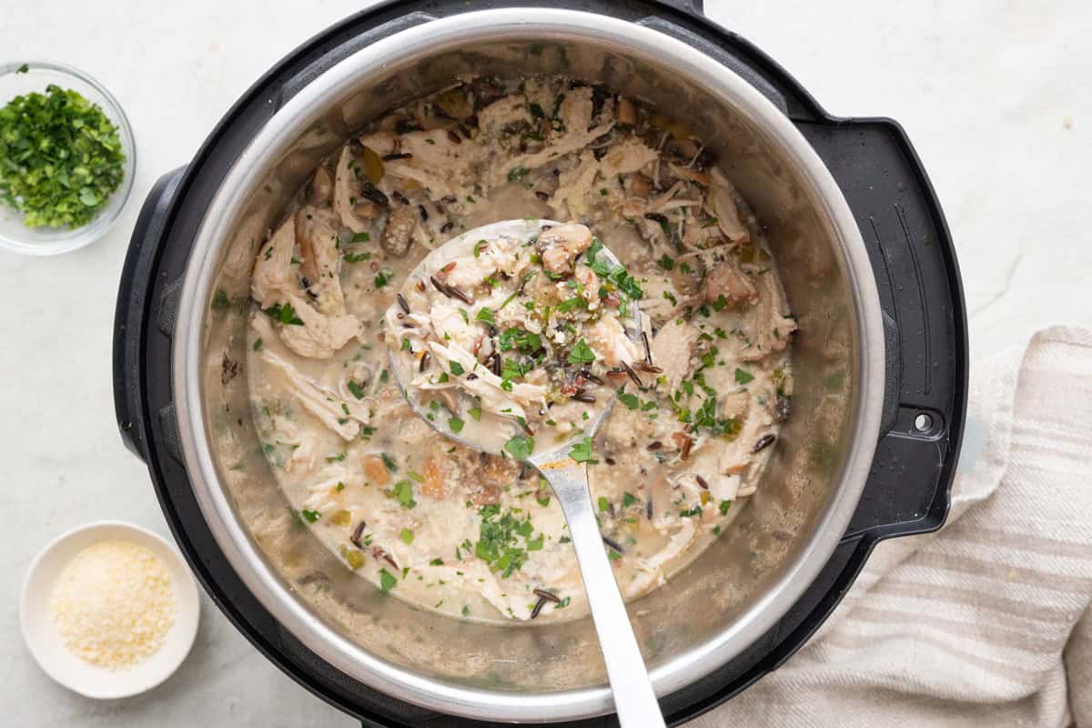 Chicken and rice in IP with a spoon dipped in, garnished with fresh parsley and parmesan cheese.