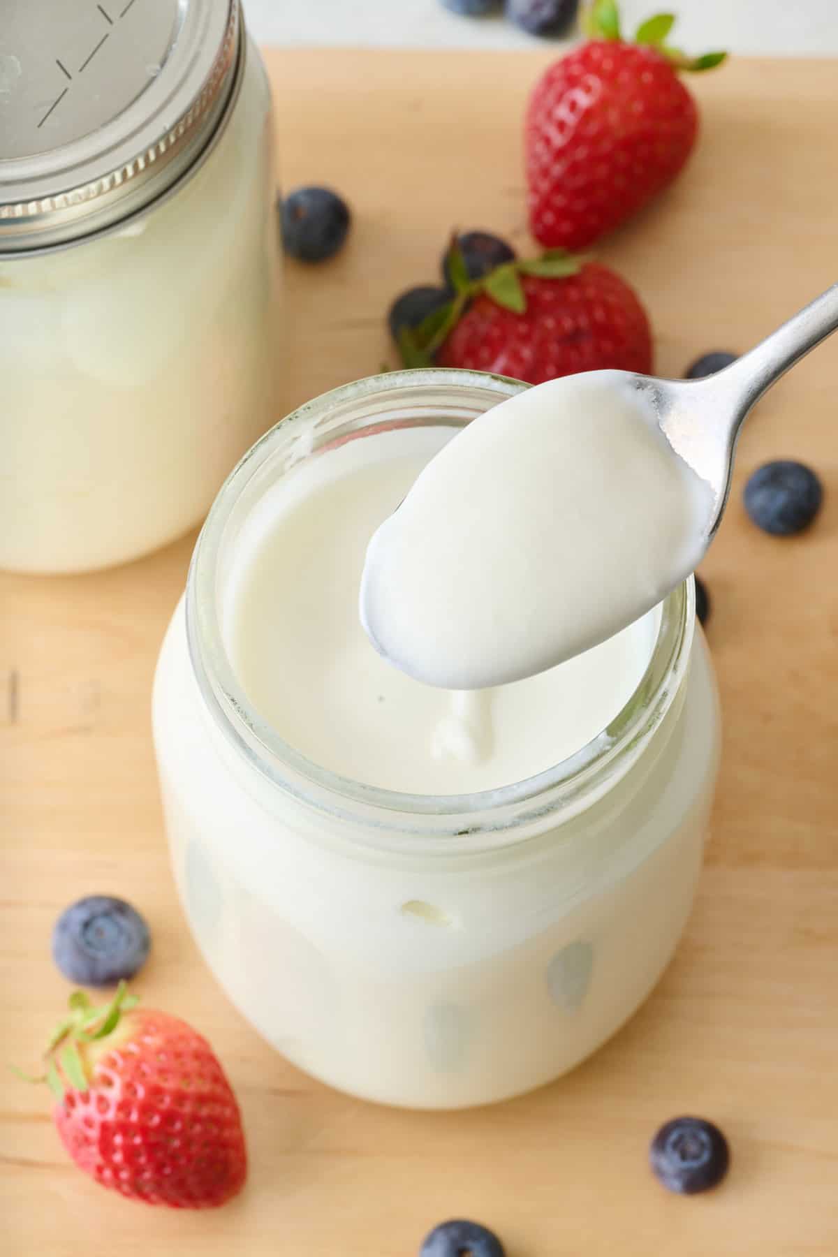 Spoon scooping up Instant Pot yogurt from a mason jar surrounded by strawberries and blueberries.