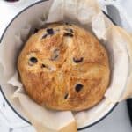 Baked olive bread on parchment paper in a dutch oven.