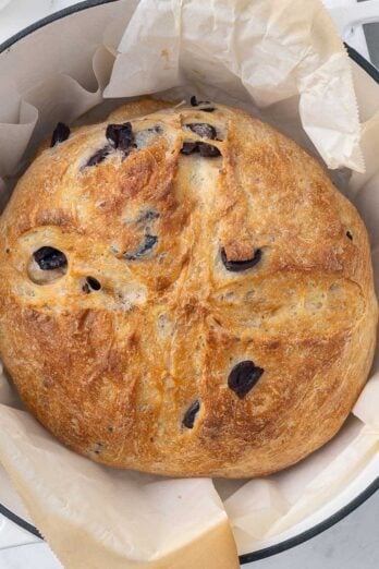 Baked olive bread on parchment paper in a dutch oven.