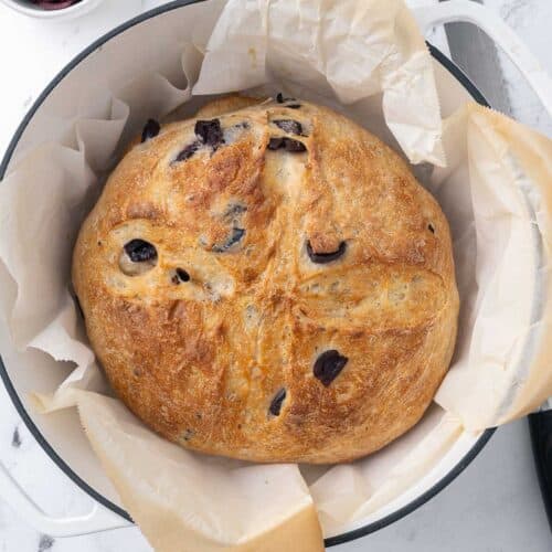 Baked olive bread on parchment paper in a dutch oven.