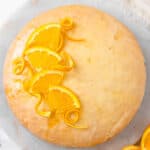 Closeup of glazed orange cake garnished with orange slices and spiraled peels.