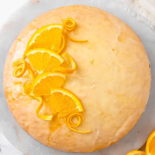Closeup of glazed orange cake garnished with orange slices and spiraled peels.