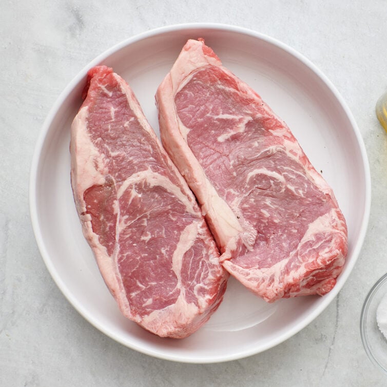 Ingredients for recipe: NY strip steak, salt, black pepper, olive oil, unsalted butter, sprigs of rosemary.