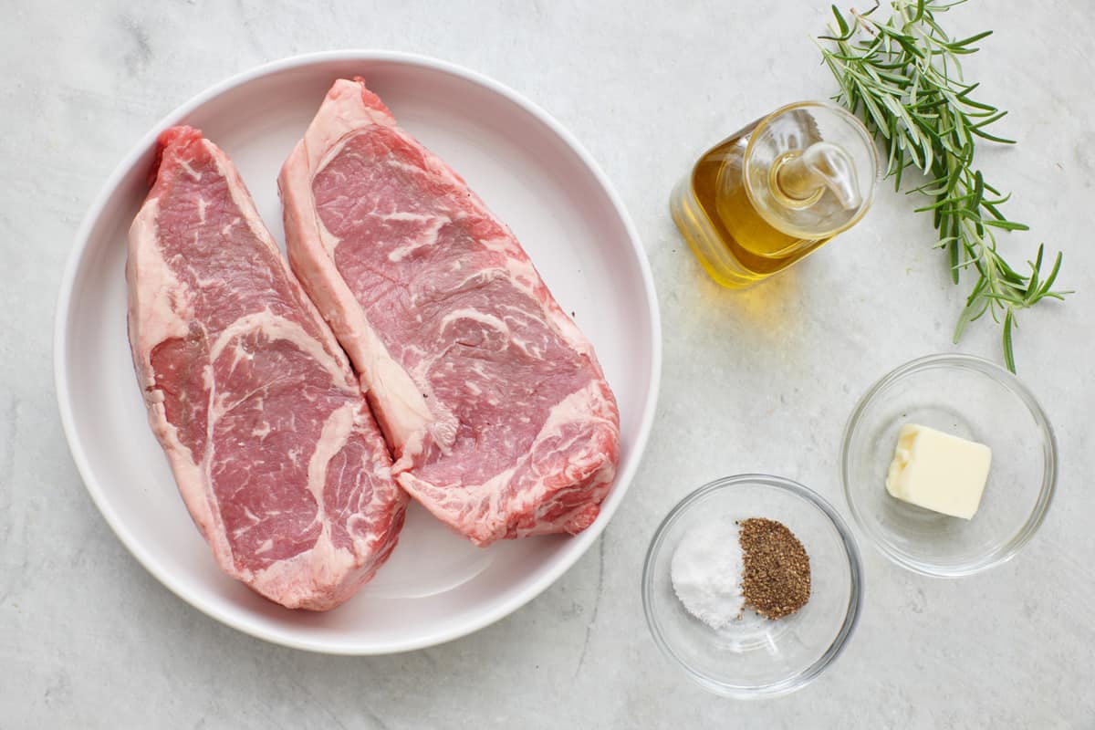 Ingredients for recipe: NY strip steak, salt, black pepper, olive oil, unsalted butter, sprigs of rosemary.