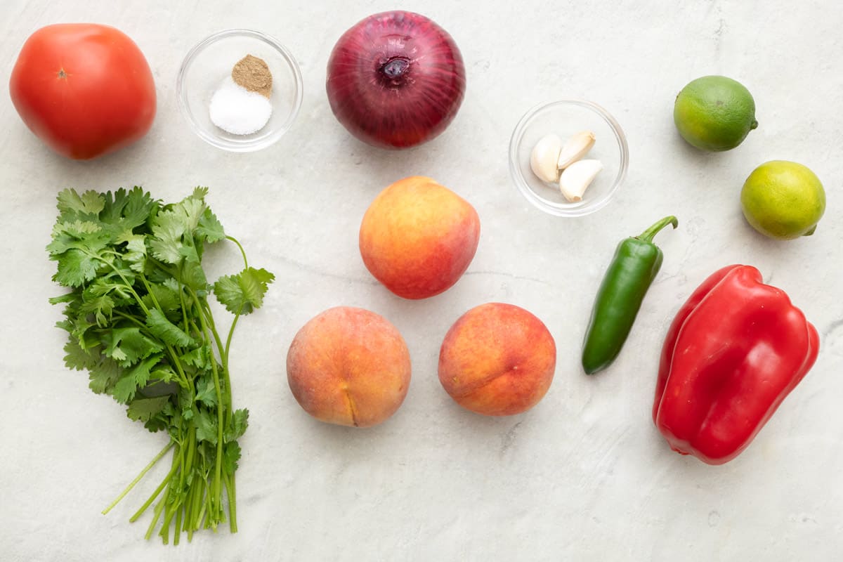 Ingredients to make recipe: Tomato, salt, pepper, red onion, garlic cloves, limes, peaches, jalapeรฑo, and red bell pepper.
