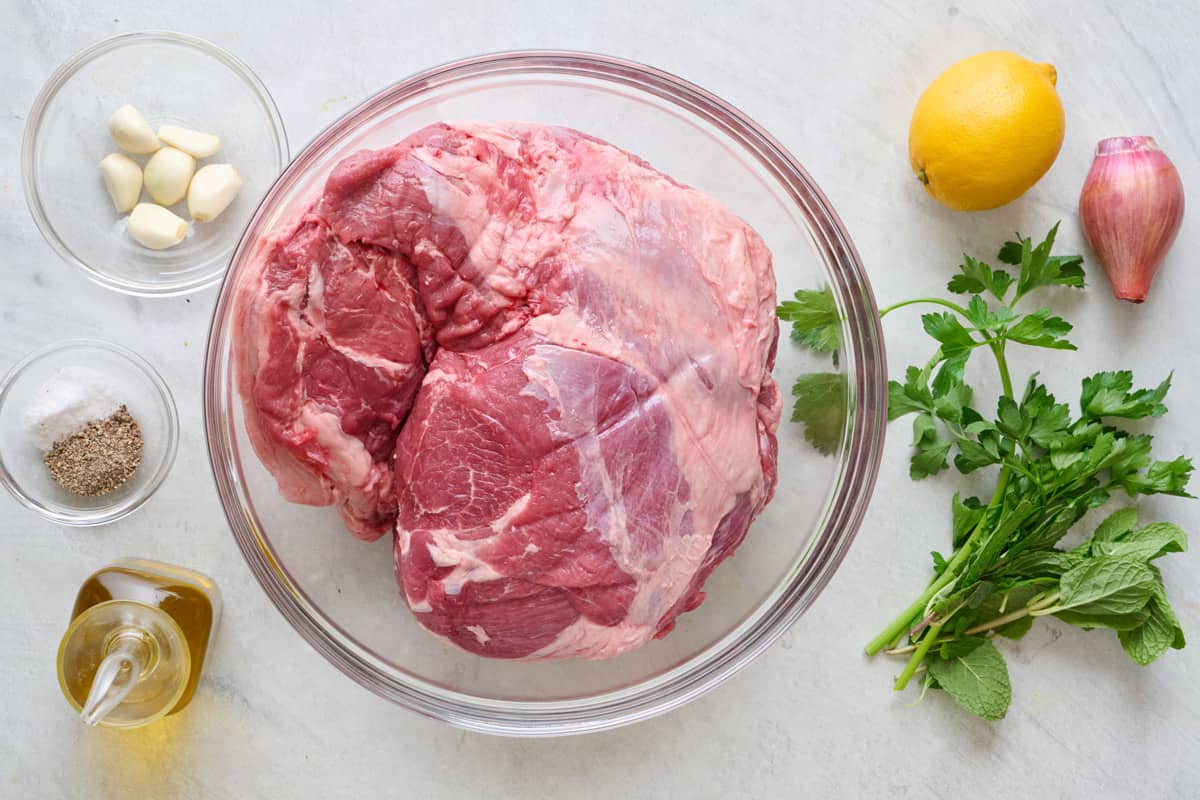 Ingredients for recipe: Leg of lamb roast, garlic cloves, lemon, shallot, olive oil, salt, black pepper, fresh parsley, and fresh mint.