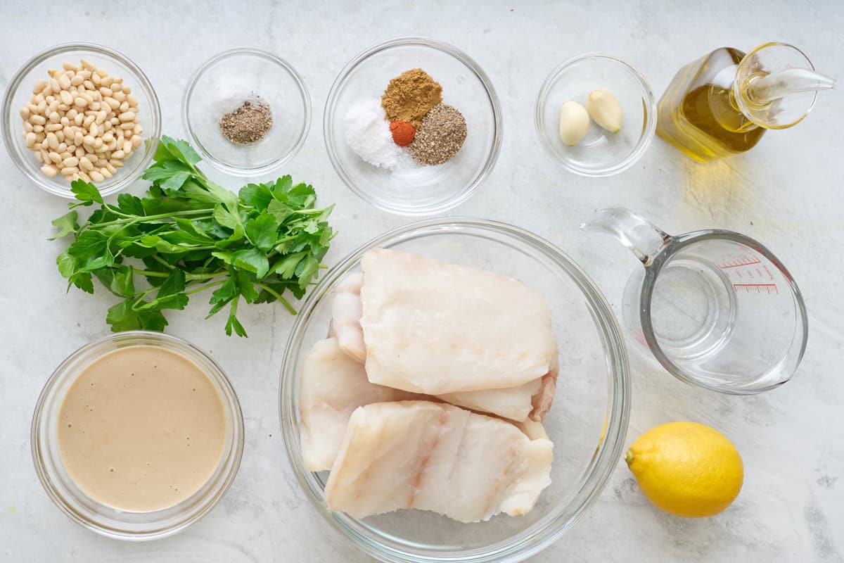 Ingredients for recipe: Cod fish fillets, tahini paste, lemon juice, garlic cloves, water, salt, cumin, black pepper, cayenne pepper, olive oil, pine nuts, fresh parsley.