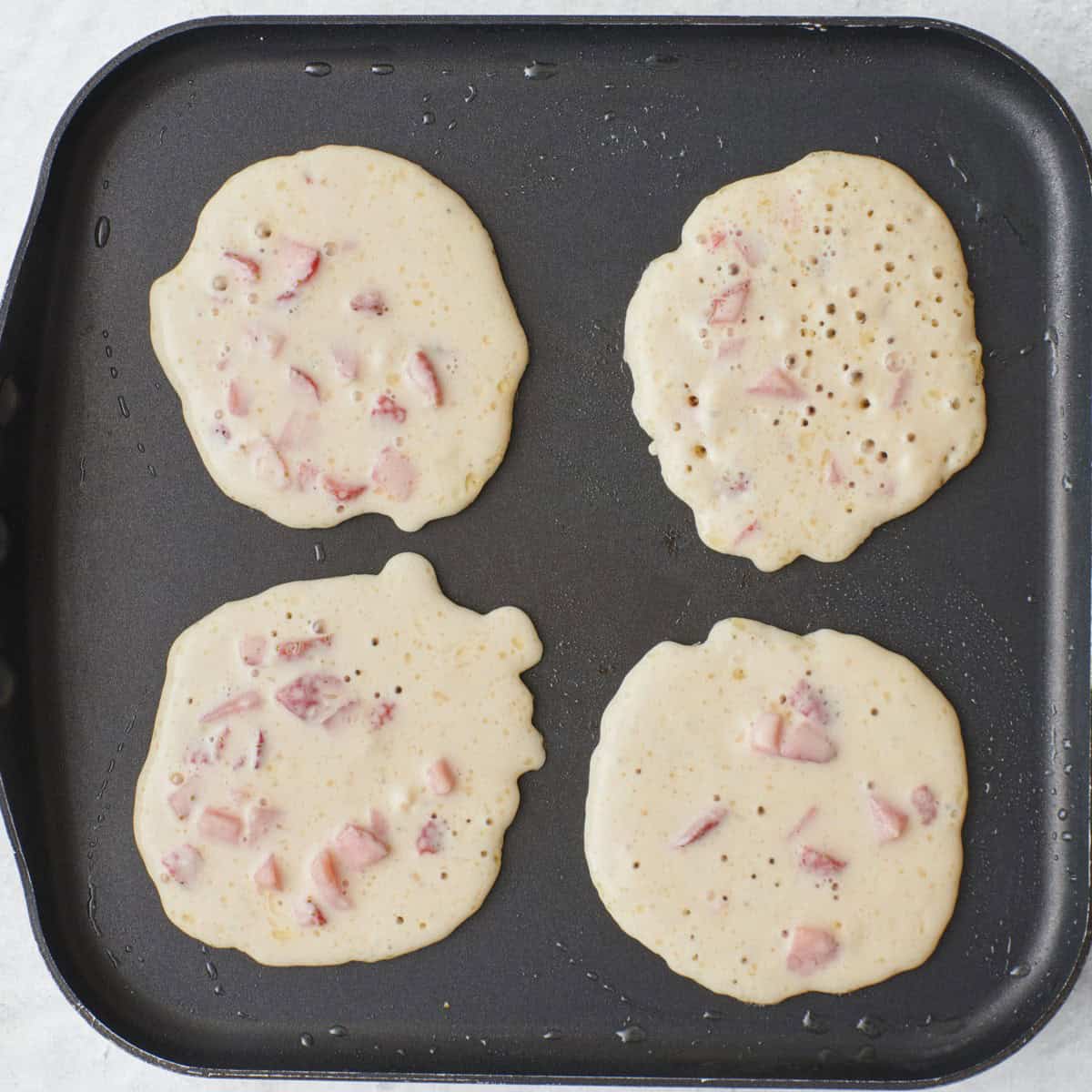 Batter on a pan, making four pancakes.