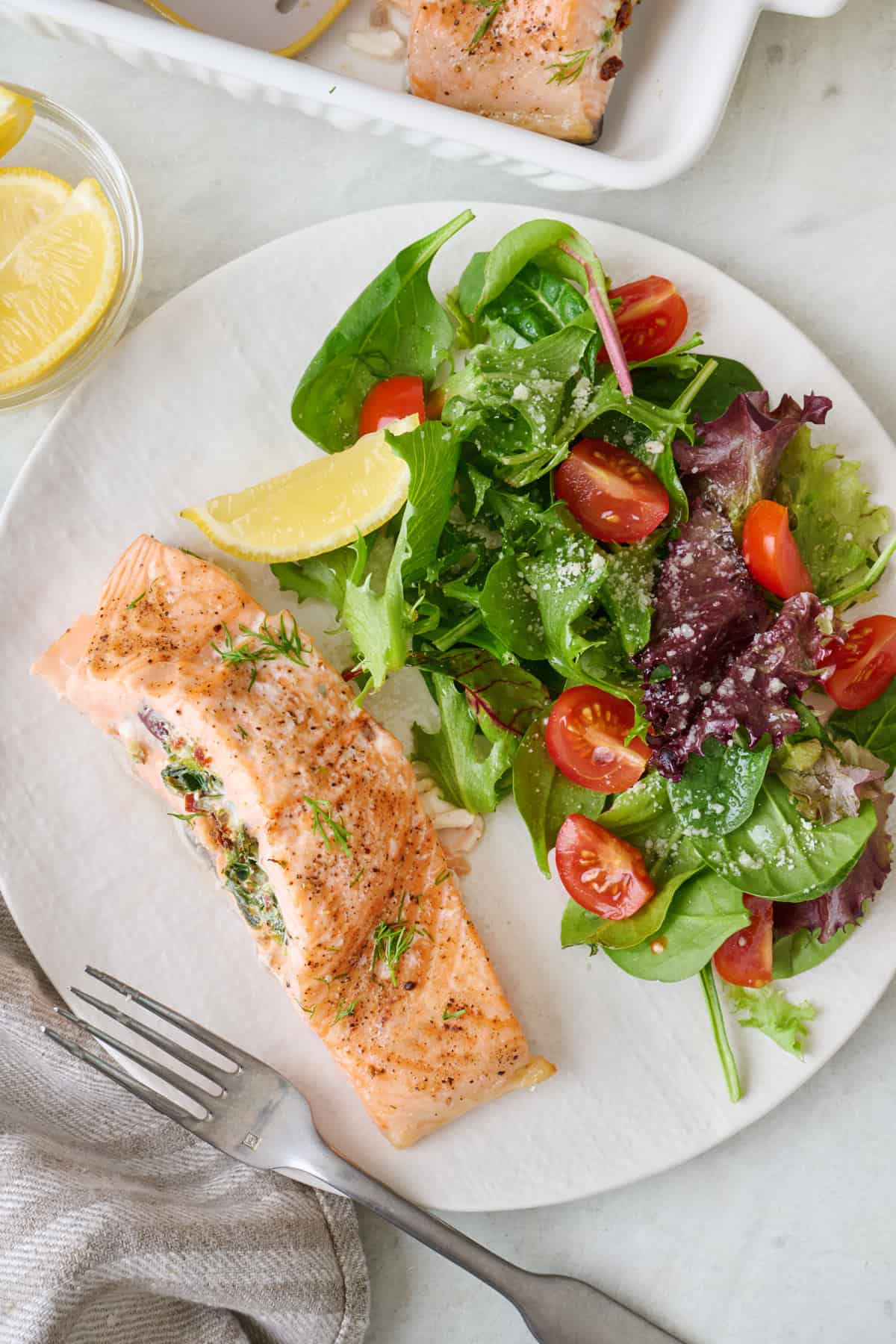 Stuffed salmon on a white plate with a side salad, lemon slice, and a fork.