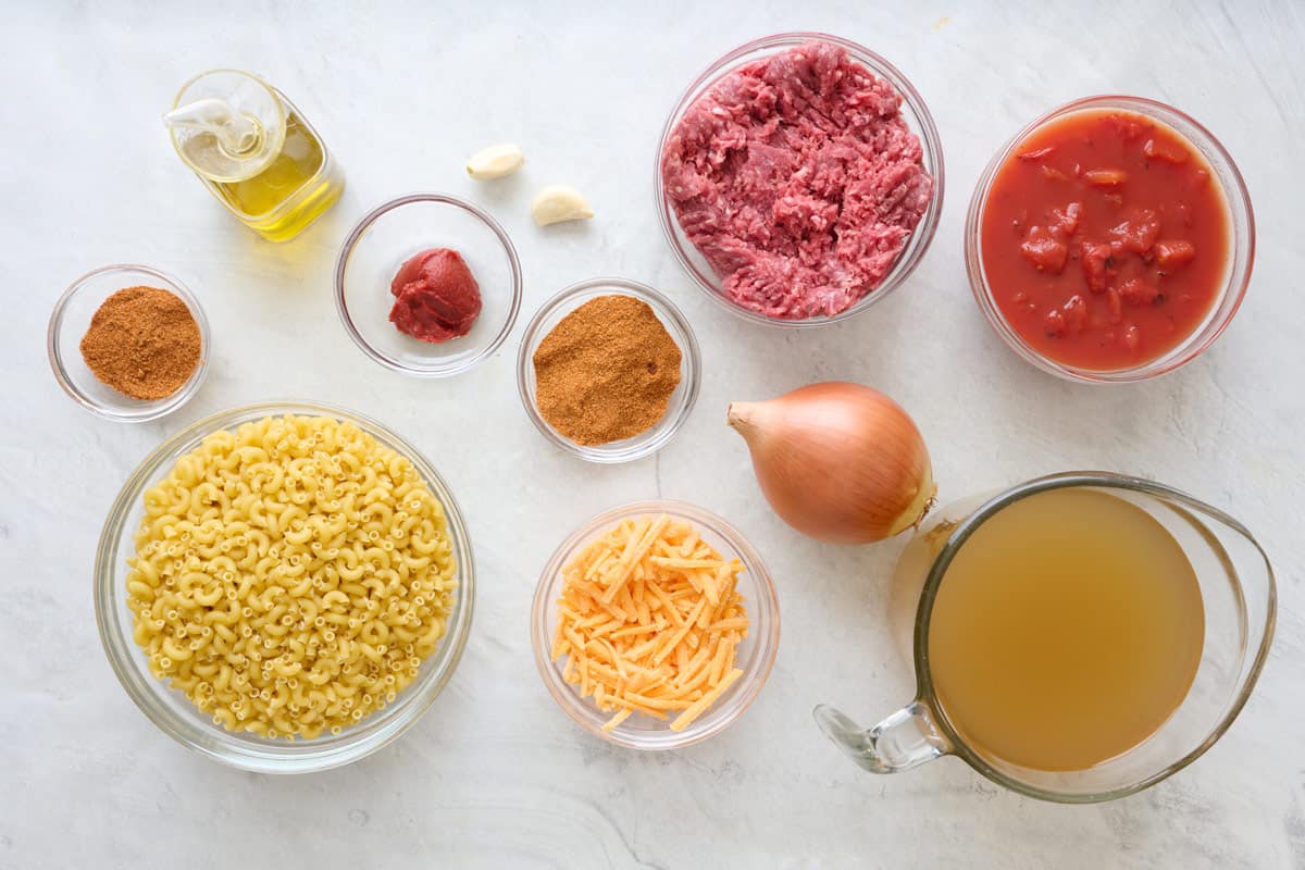 Ingredients for recipe: Ground beef, pasta, sharp cheddar cheese, olive oil, onion, garlic, taco seasoning, tomato paste, fire-roasted tomatoes, and chicken stock.