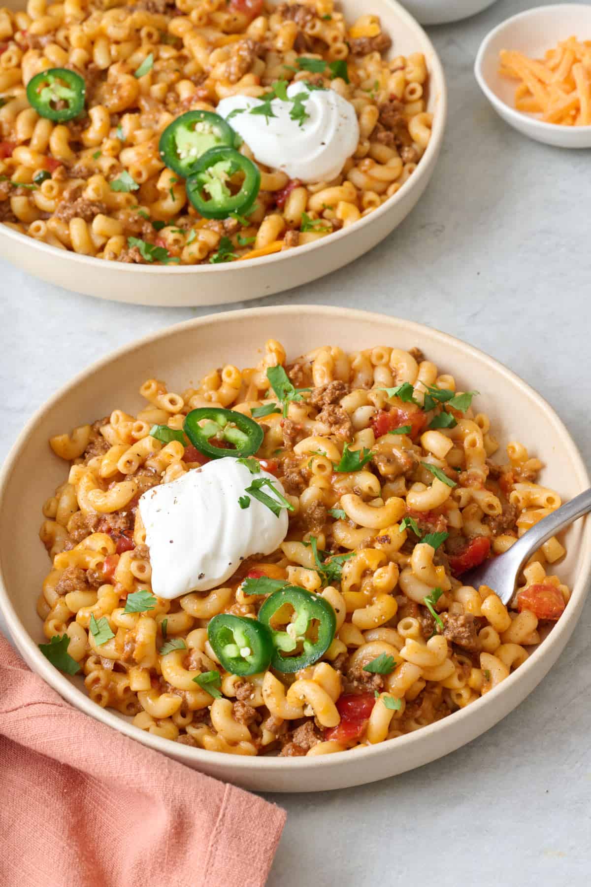 2 bowls of taco pasta with sour cream, jalapeรฑos, and fresh cilantro on top.