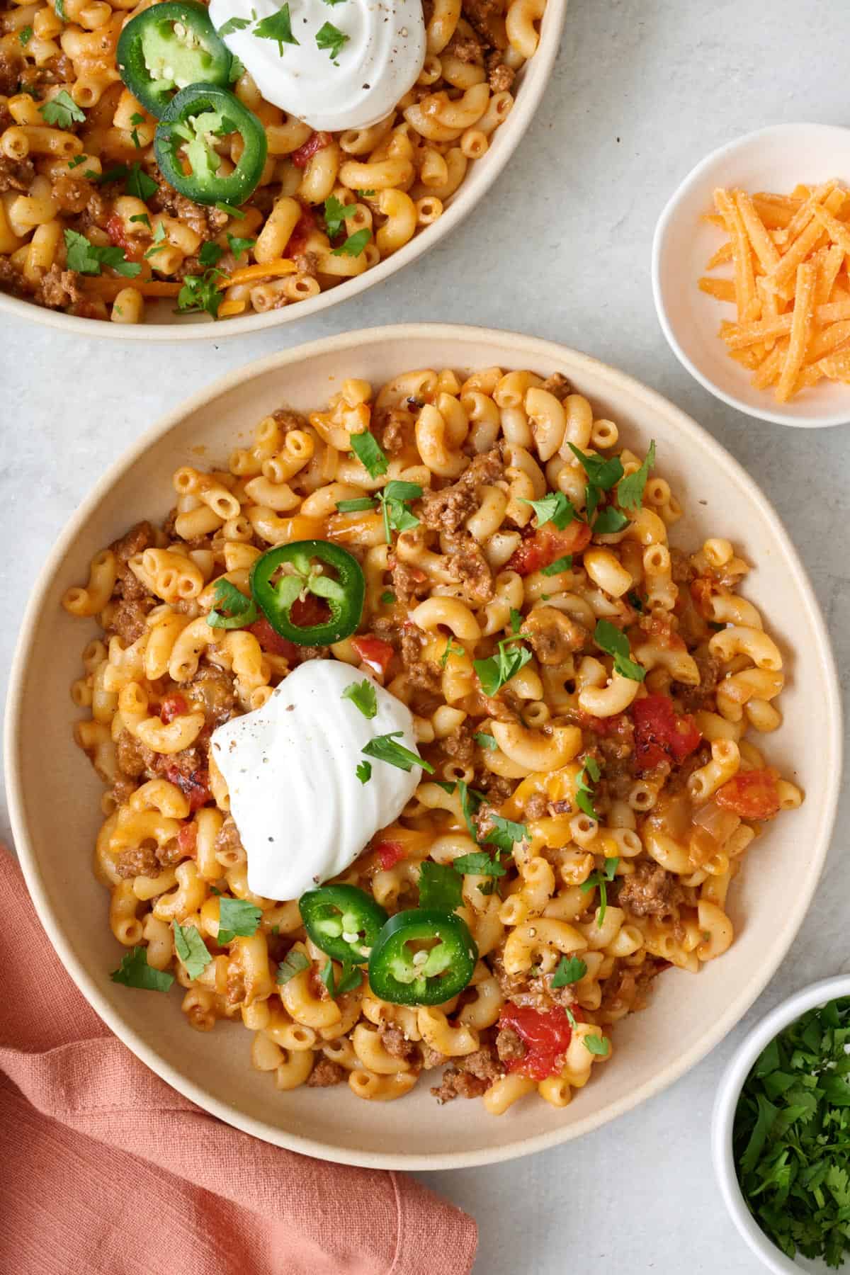 Bowl of taco pasta topped with a dollop of sour cream, jalapeรฑos, and fresh cilantro with another bowl nearby.