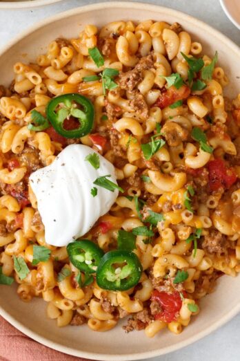 Closeup of bowl of taco pasta topped with jalapeños, fresh cilantro, and a dollop of sour cream.