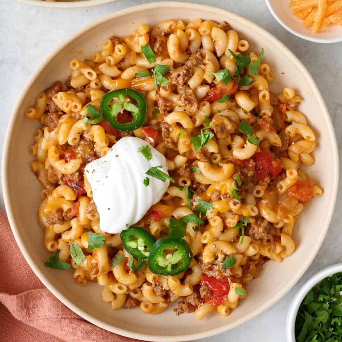 Closeup of bowl of taco pasta topped with jalapeรฑos, fresh cilantro, and a dollop of sour cream.