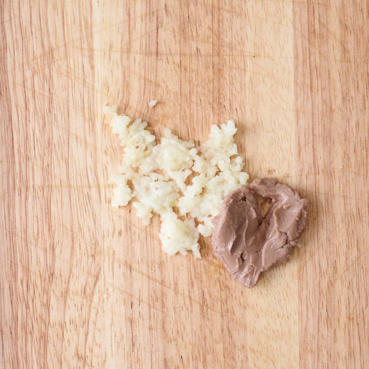Minced garlic and anchovy paste on a wooden cutting board.