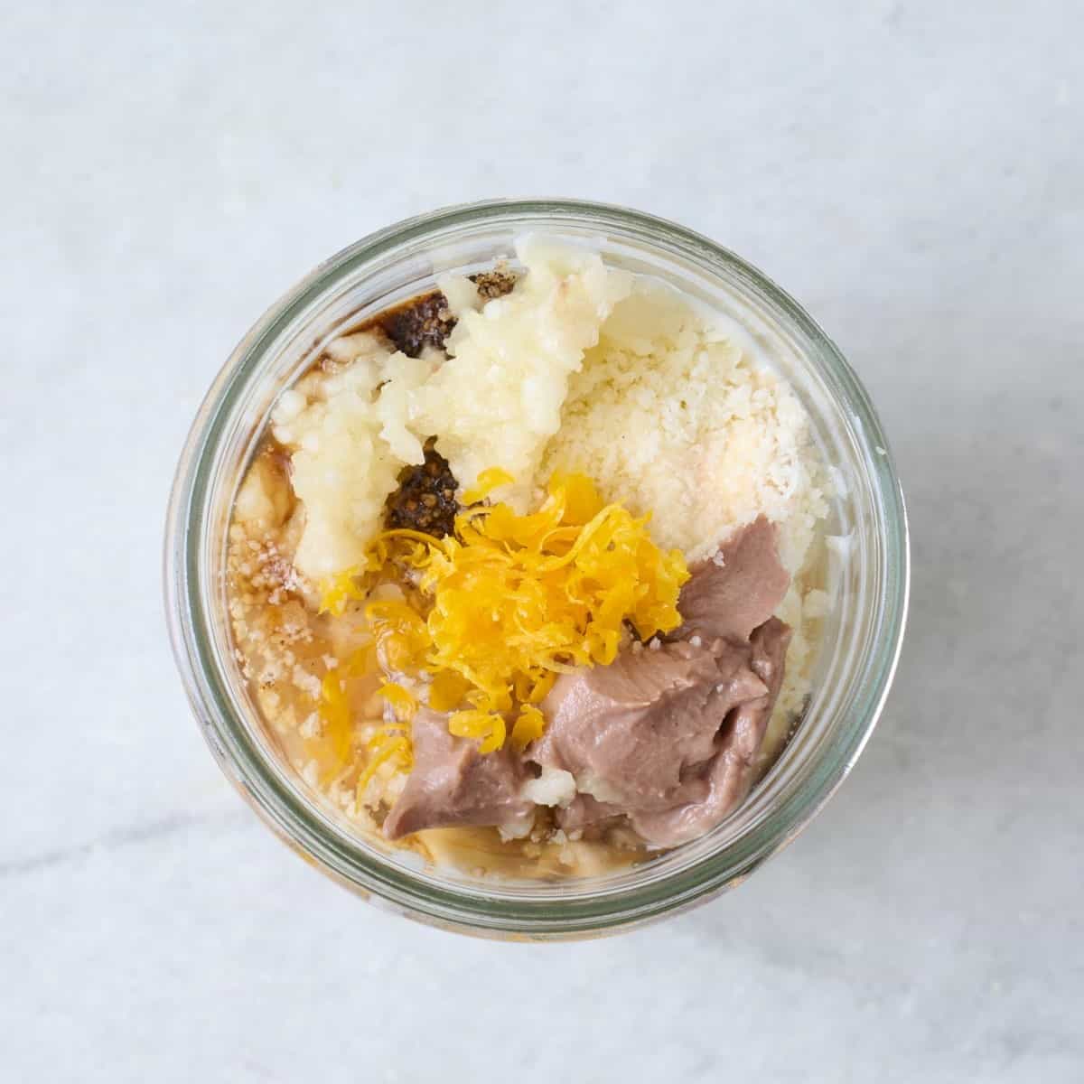 Caesar dressing ingredients unmixed in a small glass jar.