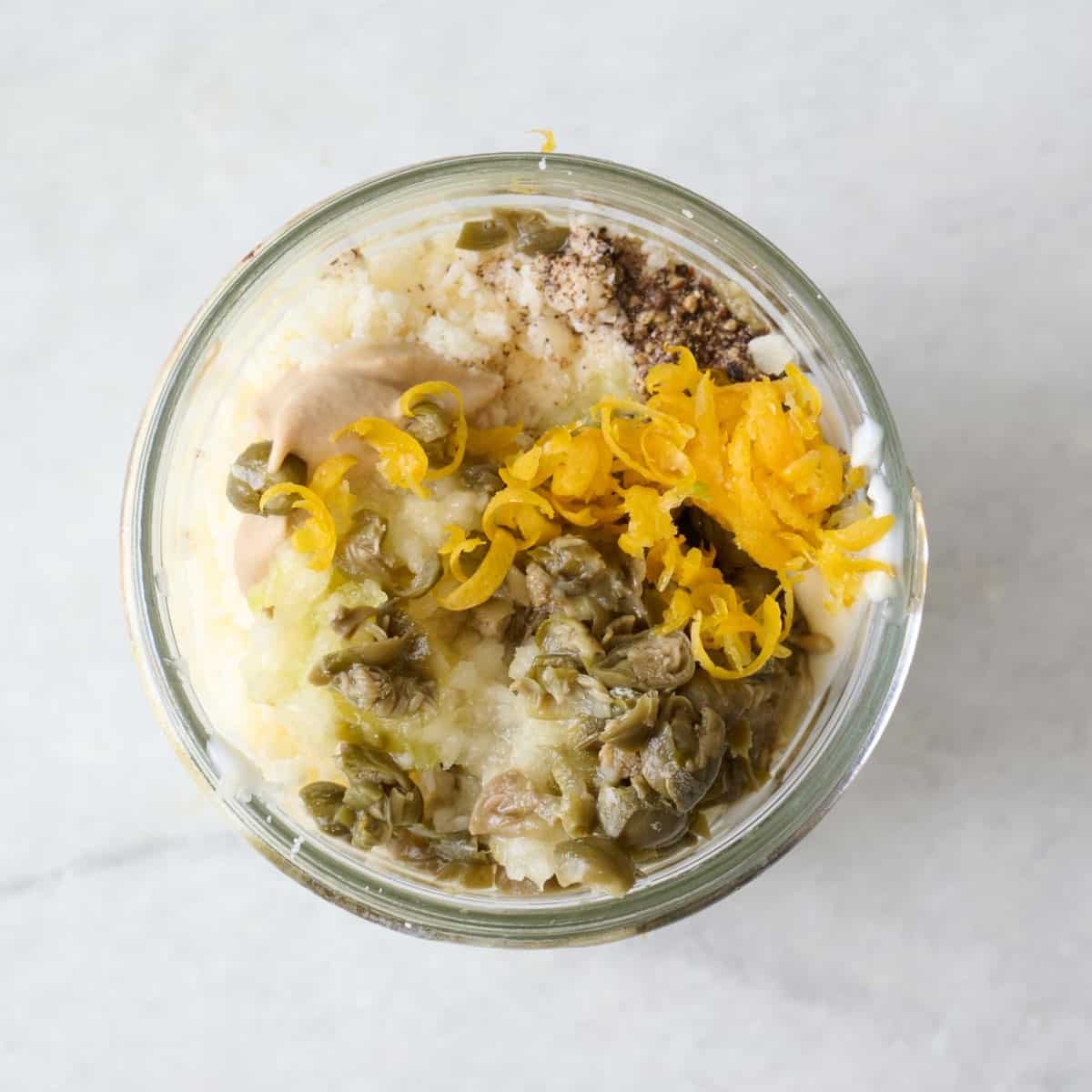 Caesar dressing ingredients unmixed in a small glass jar.