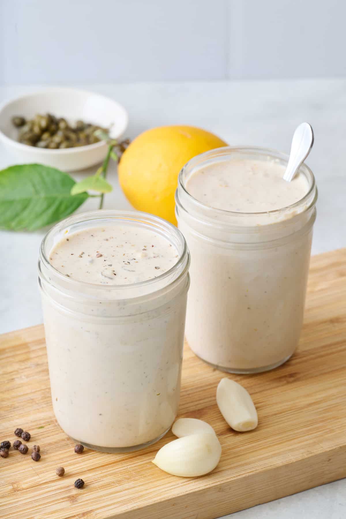 Two jars of Caesar salad dressing on a wooden cutting board.