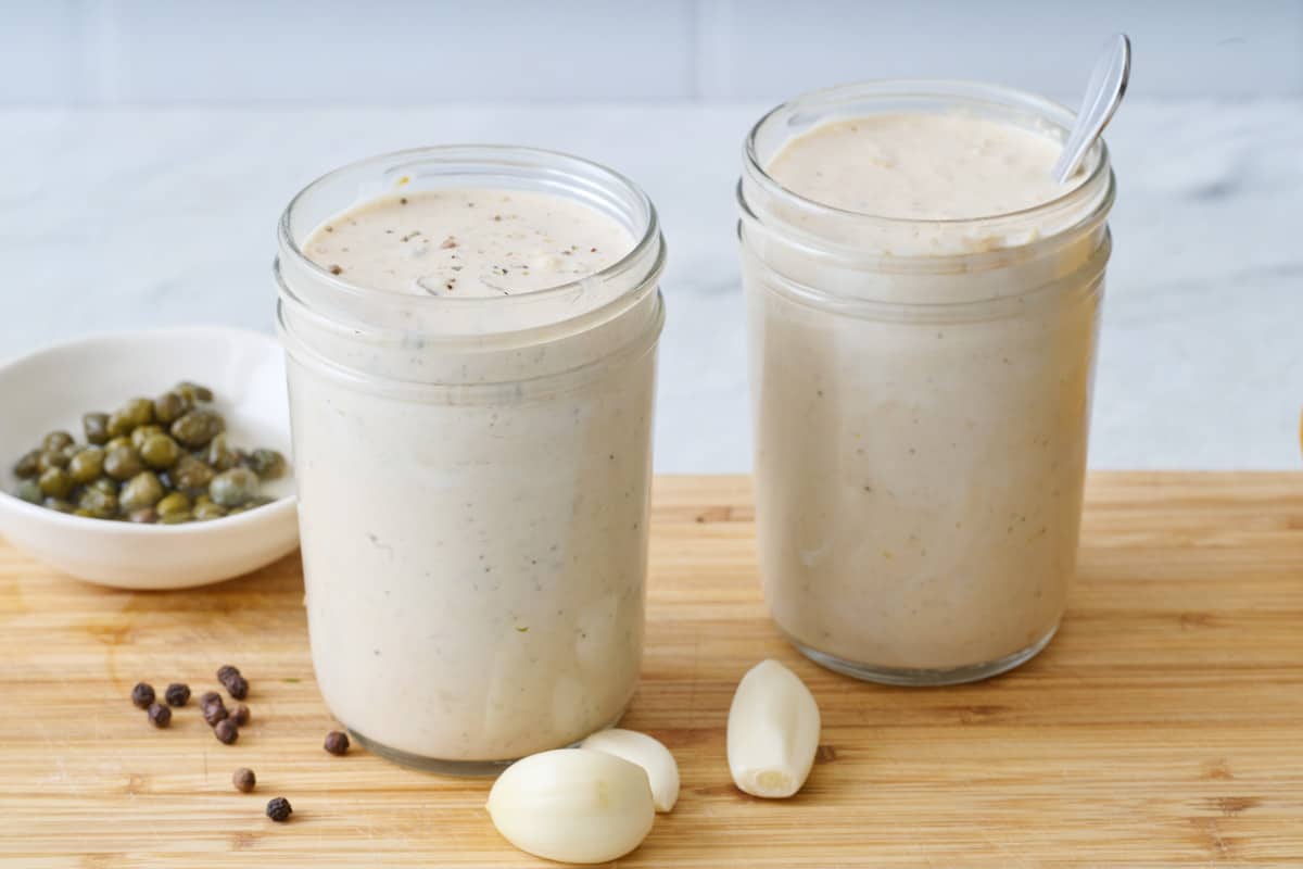 Two jars of Caesar salad dressing on a wooden cutting board.