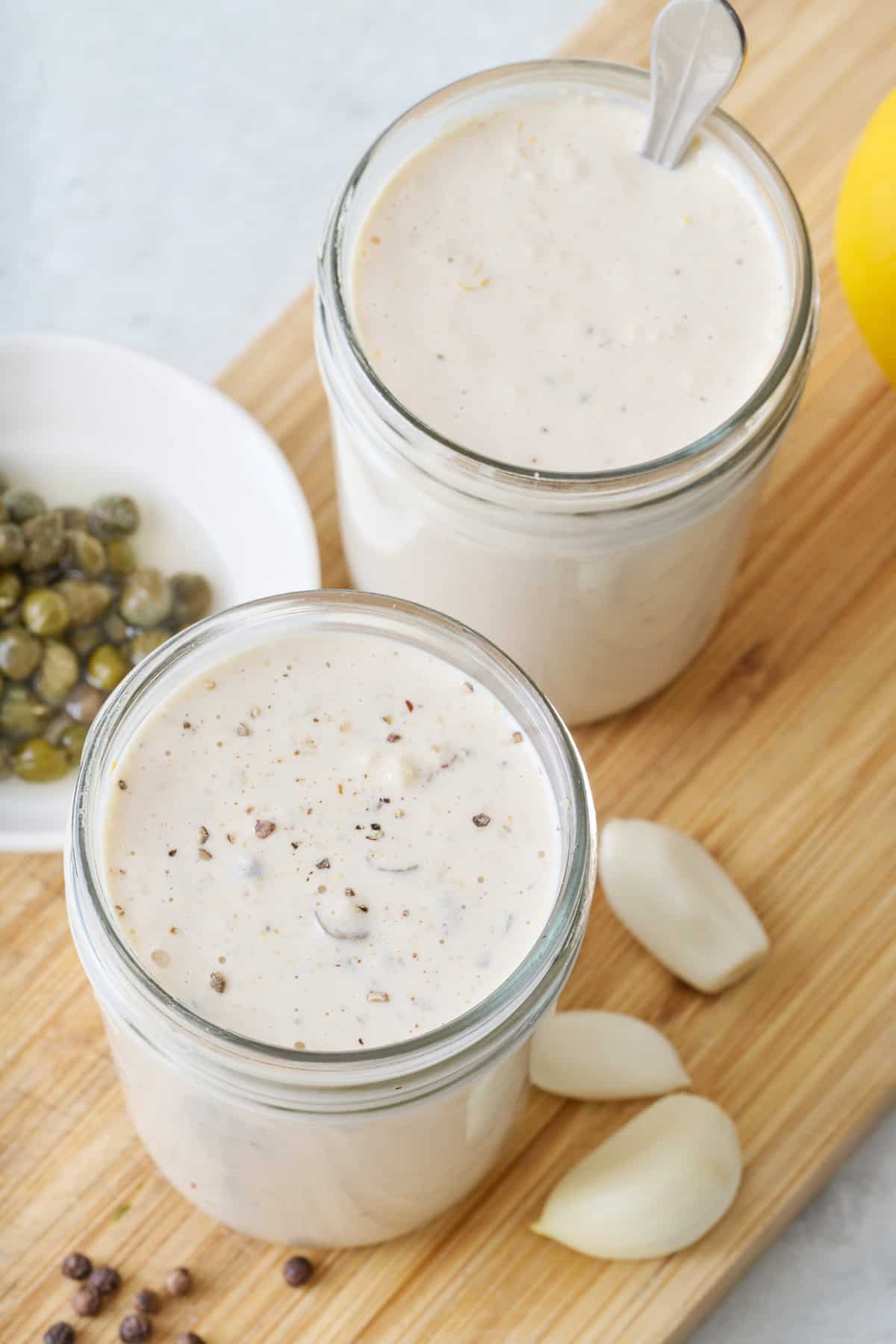 Two small glass jars of Caesar salad dressing.