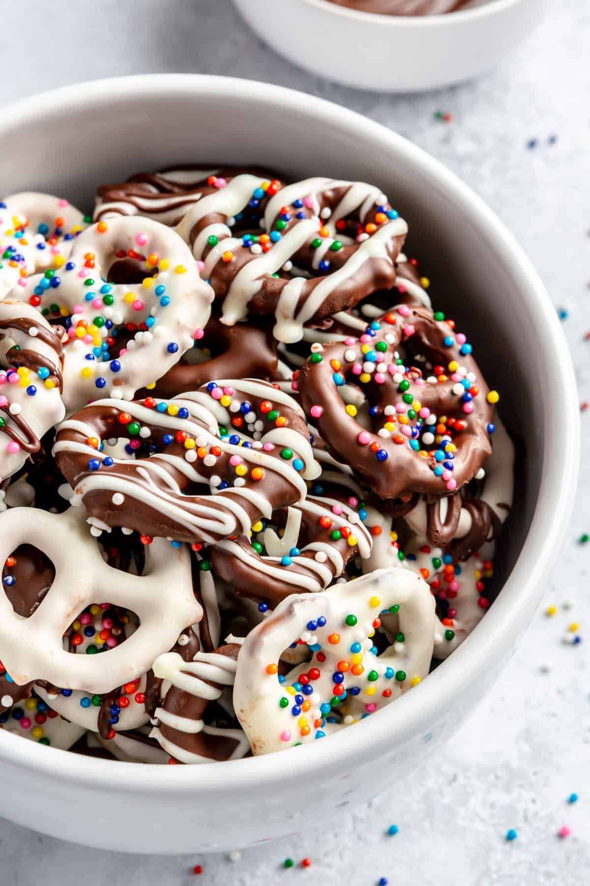 Small bowl of chocolate-covered pretzels with drizzled chocolate and rainbow sprinkles.