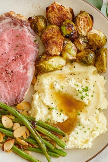 slice of prime rib, brussel sprouts, green beans, mashed potatoes on a plate