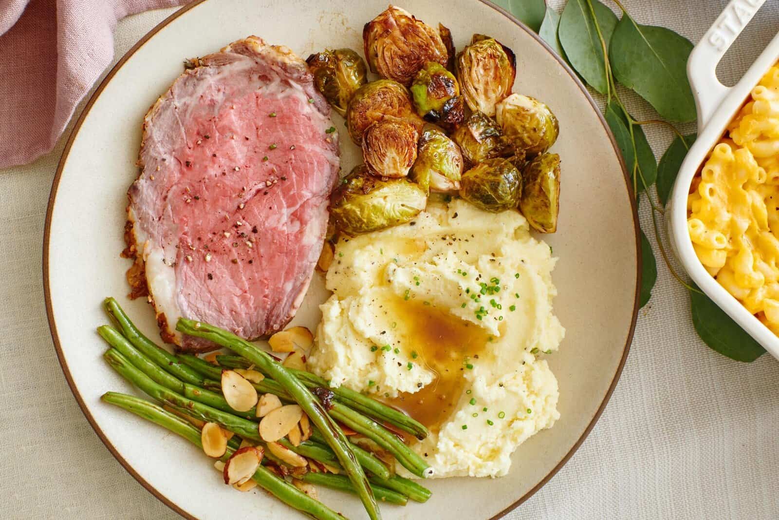 slice of prime rib, brussel sprouts, green beans, mashed potatoes on a plate