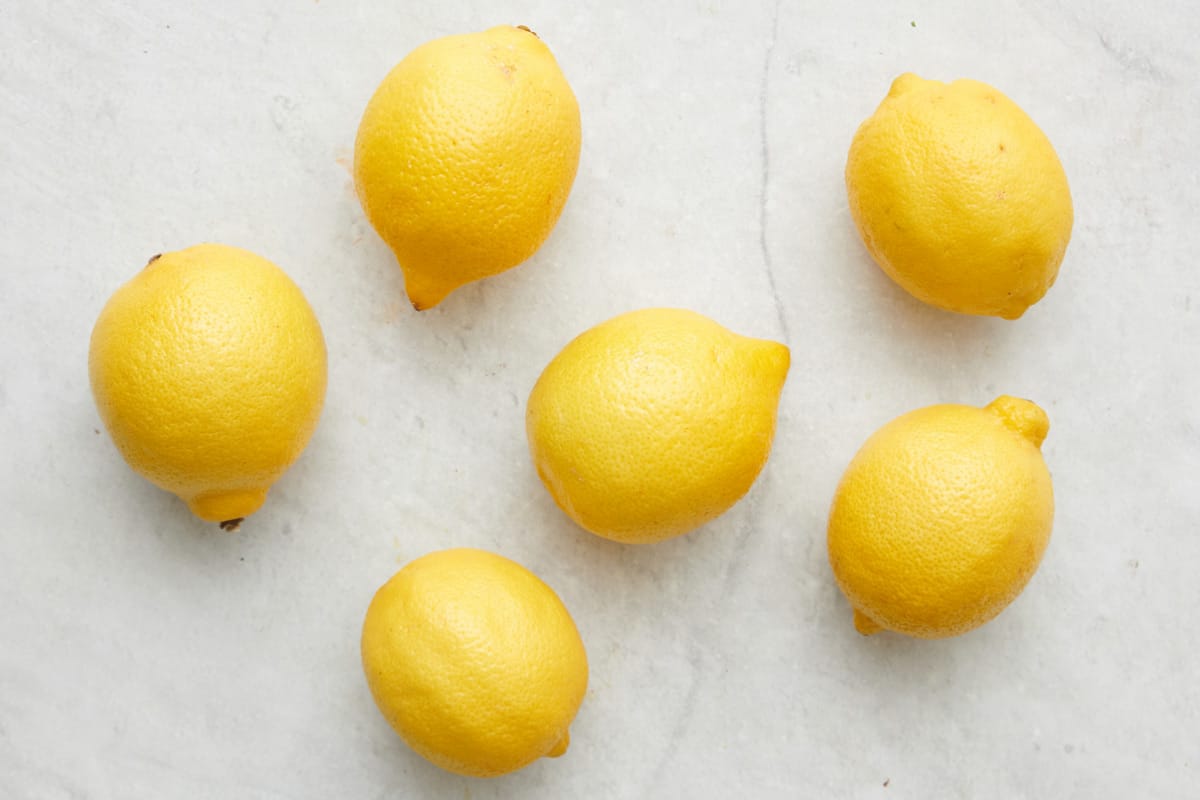 6 fresh whole lemons on a marble countertop.