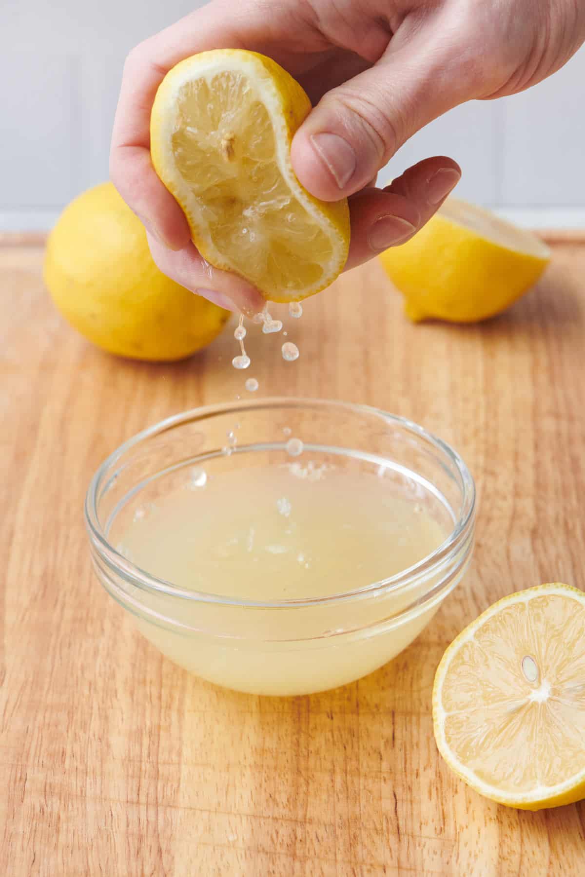 Action shot of how to juice a lemon: Hand holding half a cut lemon squeezing juice into a sieve over a bowl.