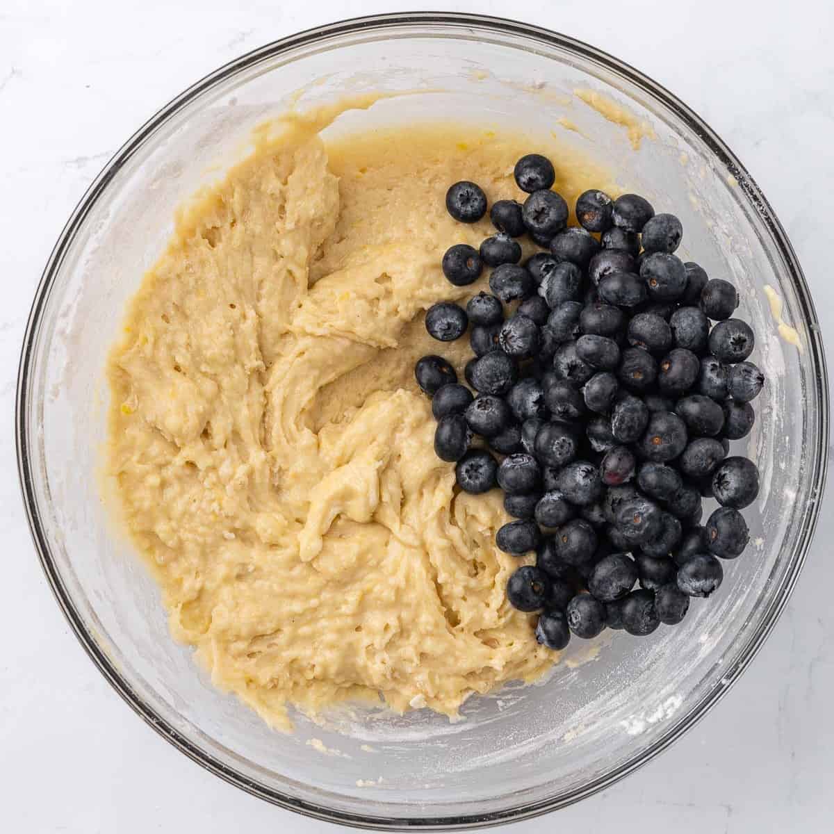 Fresh blueberries on top of batter in a large glass mixing bowl.