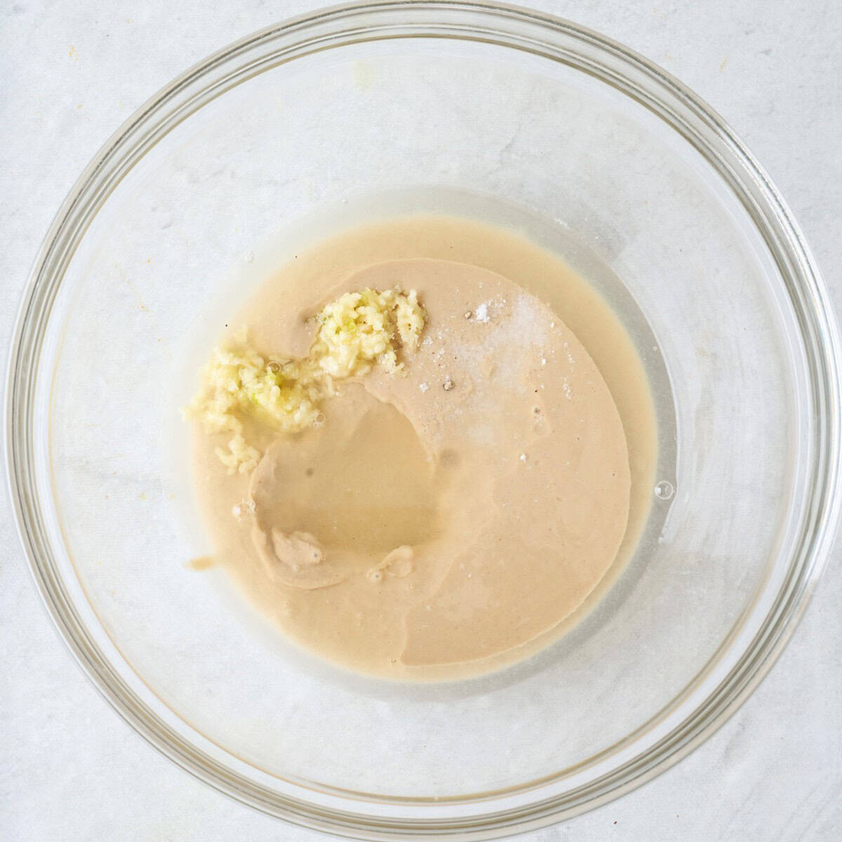 Tahini paste in a small bowl with lemon juice, garlic and salt before mixing.