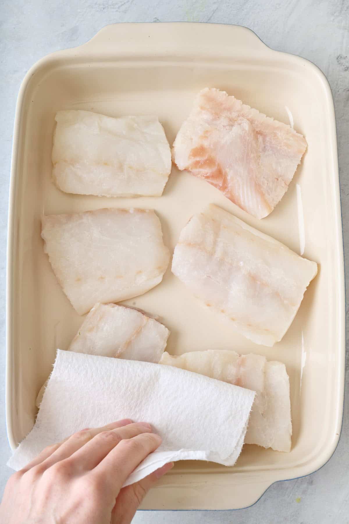 Cod fillets in a baking dish with paper towels patting them dry.