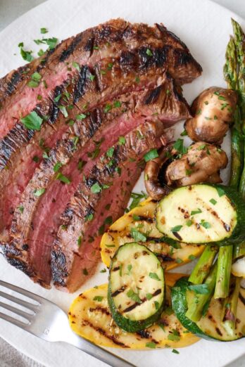 Sliced flank steak on a plate with grilled veggies.