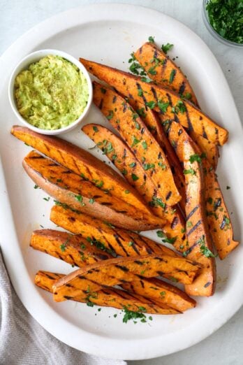 Grilled sweet potato wedges on a large platter with sauce for dipping.